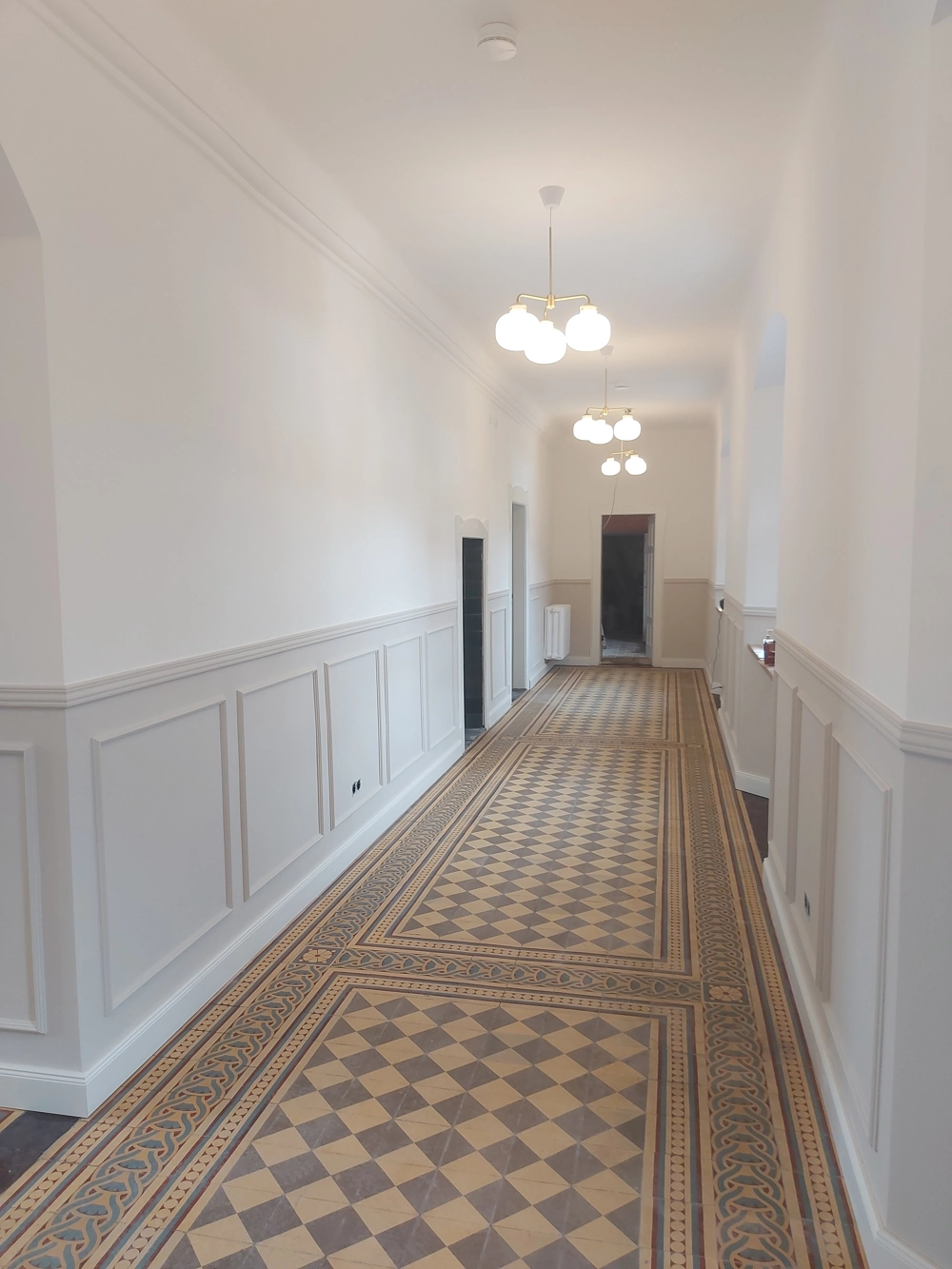 Heller Altbauflur mit weißen Wandpaneelen, neuen Deckenleuchten und dekorativ verlegten Bodenfliesen, Fliesenarbeiten