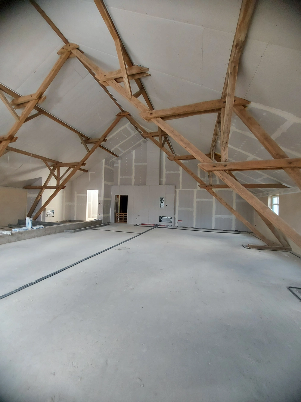 Dachbodenausbau mit sichtbaren Holzbalken, Trockenbauwänden und vorbereiteten Elektrokanälen