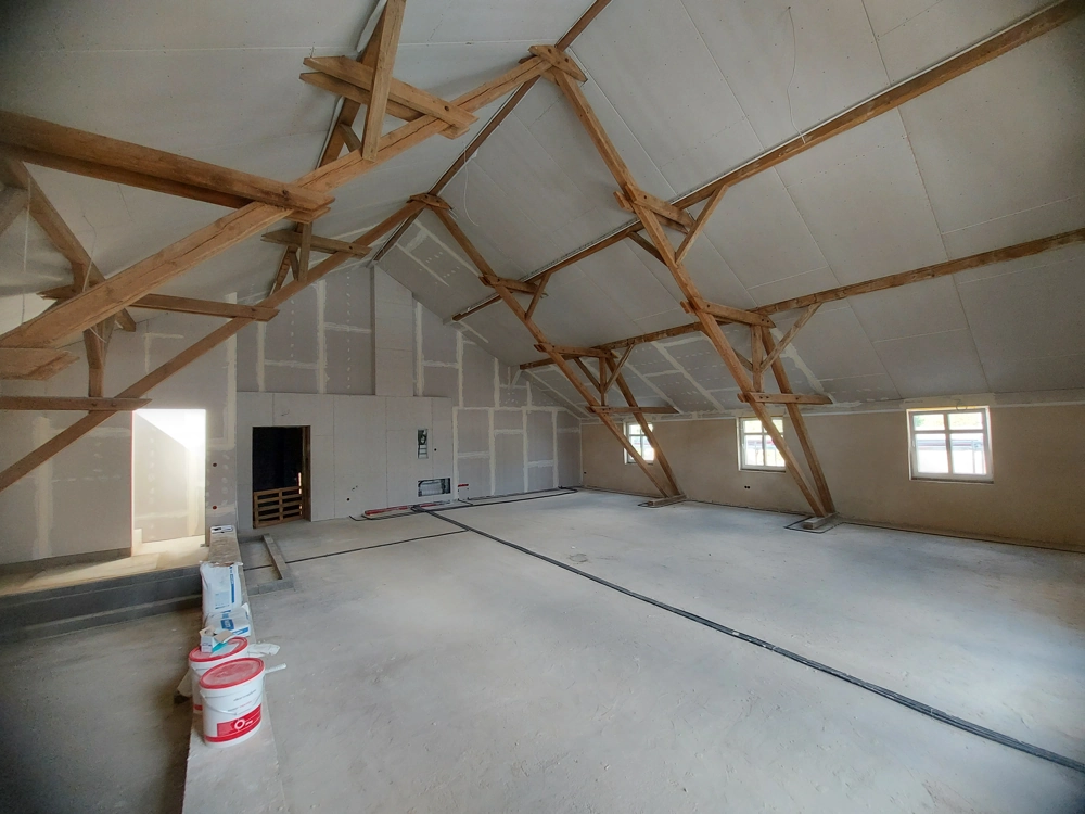 Rohboden und Spachtelmaterial im ausgebauten Dachboden mit Trockenbauwänden und sichtbaren Holzbalken