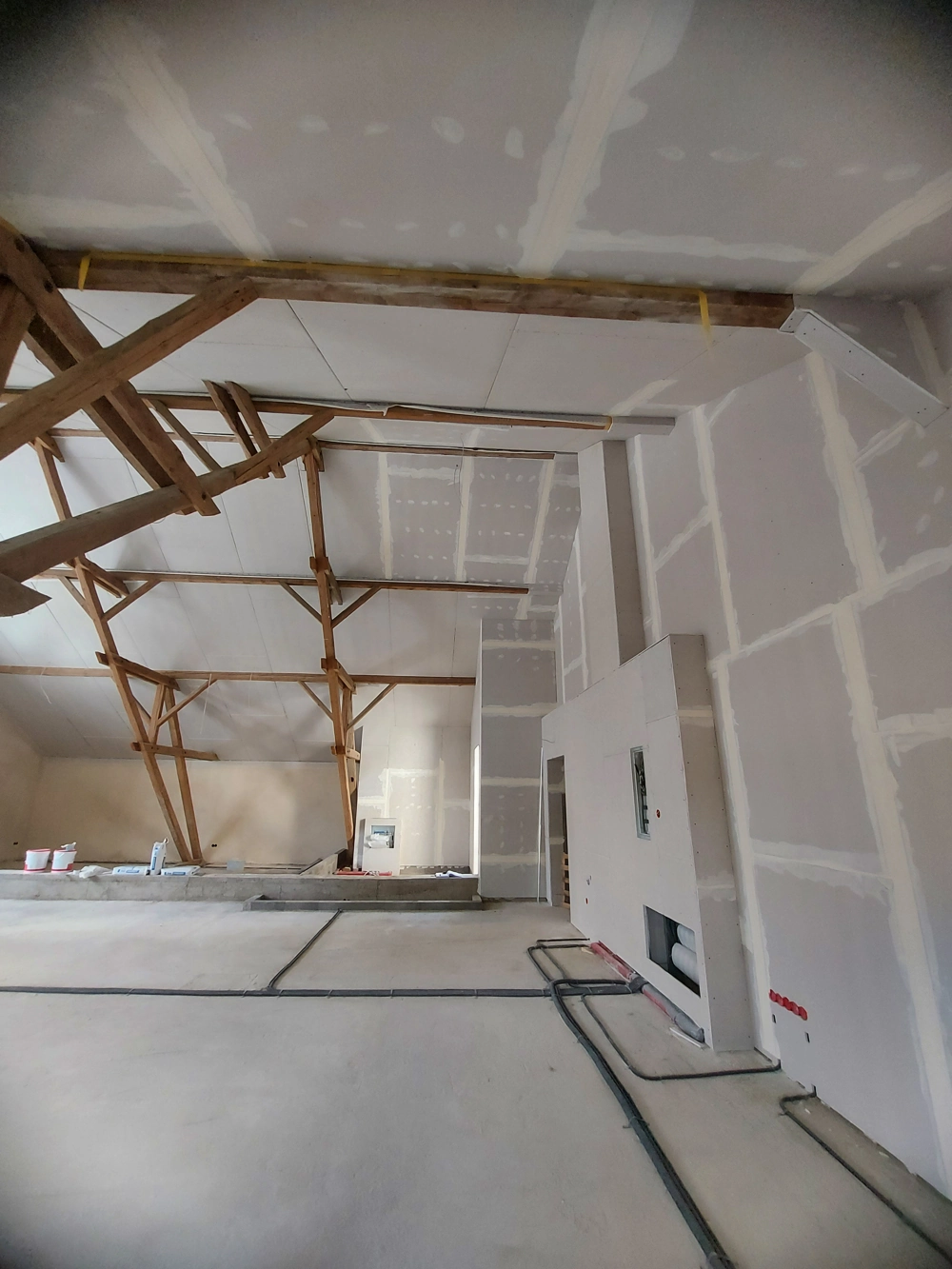 Großer Dachboden mit frisch montierten Gipskartonwänden, sichtbaren Holzbalken und Elektroinstallationen im Rahmen des Dachbodenausbaus