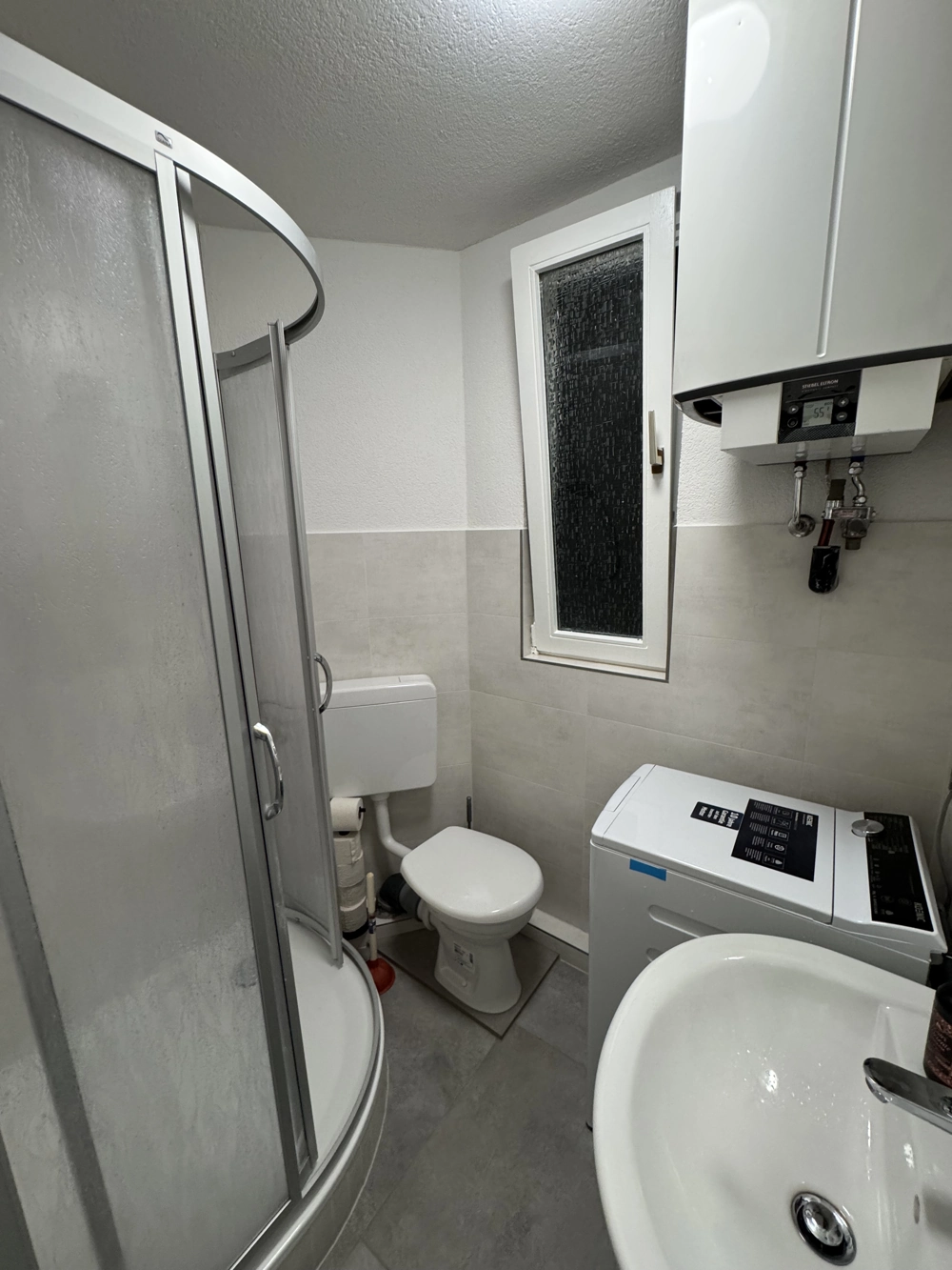 Kompaktes Bad mit Eckdusche, WC, Waschbecken, Waschmaschine und Wasserboiler nach Badrenovierung