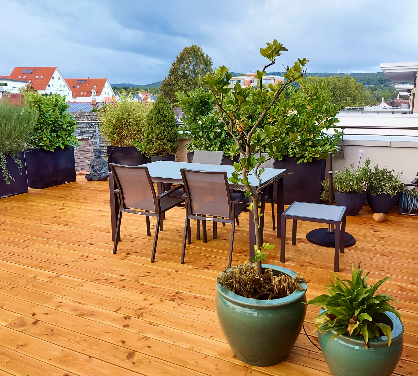 Holzterrasse mit Esstisch, Stühlen und Kübelpflanzen auf modernem Dachbalkon