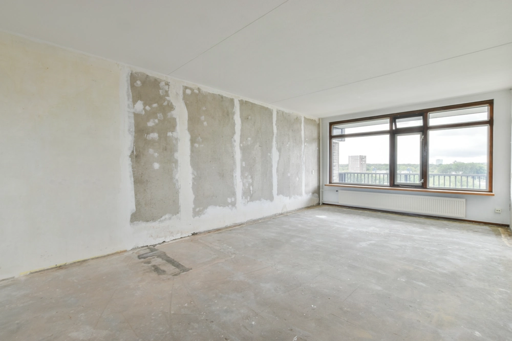 Leerer Raum mit freigelegten Wänden, Rohboden und großem Fenster – Wohnungsrenovierung