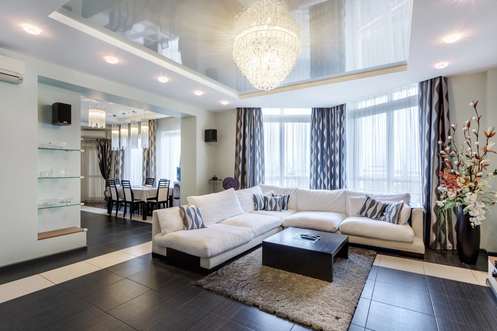 Helles Wohnzimmer mit Ecksofa, dunklen Bodenfliesen, Essbereich und Stuckdecke – Fliesenarbeiten