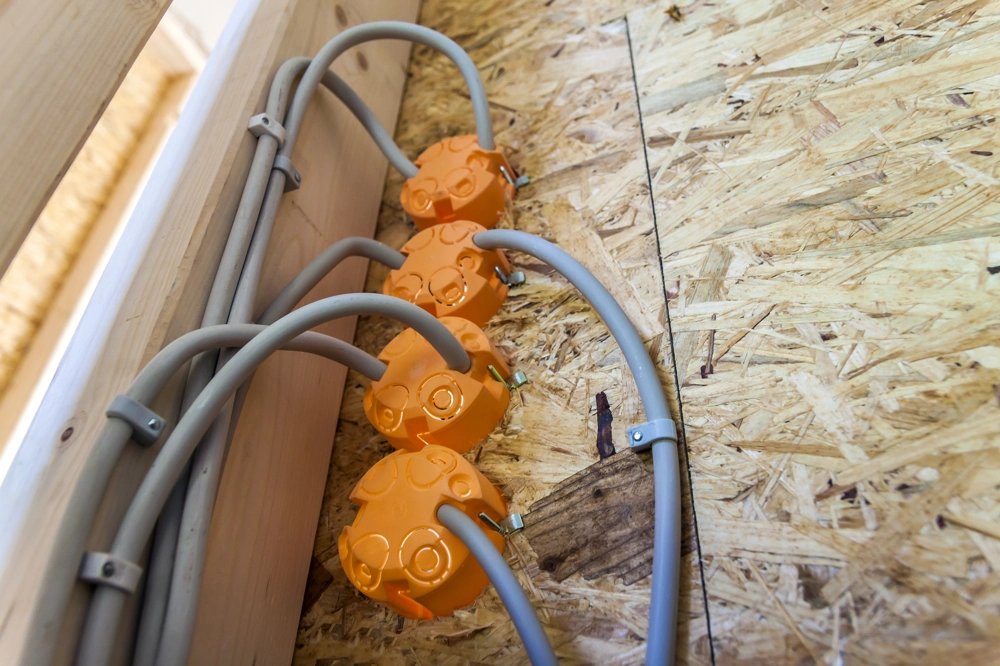 Vier orange Kabeldosen mit grauen Leitungen an OSB-Wand im Rahmen der Elektroinstallation